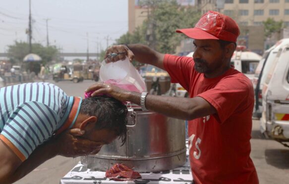 A volunteer pours water on a pedestrian during a heatwave in Karachi, Pakistan, 2022. Image ID: 2J8JH4E.