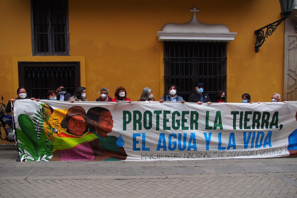 Activists holding a ban saying “Protecting Land, Water and Life”, during a protest demanding the Peruvian government to sign the Escazú Agreement to protect environmental defenders. Credit: Fotoholica Press Agency / Alamy Stock Photo. Image ID: 2JPJFGB.