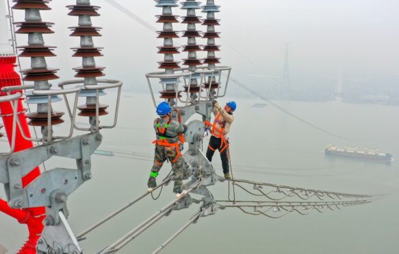 Construction workers inspect power transmission tower.