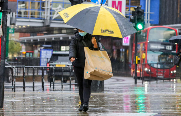 A-shopper-wearing-a-face-mask-shelters-from-the-rain-underneath-an-umbrella-on-a-wet-and-windy-day-caused-by-Storm-Alex