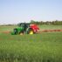 A tractor-drawn applicator applies nitrogen granule fertiliser to a field of corn.