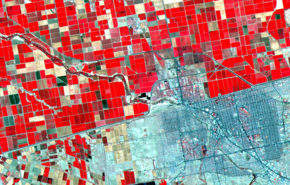 Satellite image showing the Dramatic differences in land use patterns on the US - Mexico border. Lush, regularly gridded agricultural fields on the U.S. side contrast with the more barren fields of Mexico.