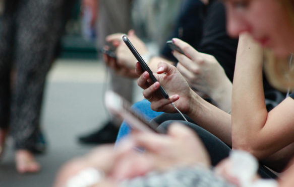 Smart phone users wait at a train station.